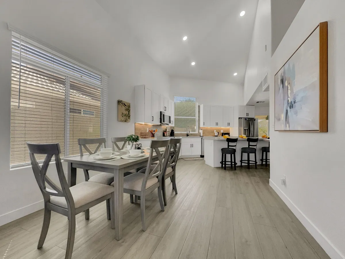A stylish dining table is set for a meal, with modern kitchen appliances and a work of art on the wall providing a sophisticated backdrop. The scene is bathed in natural light, giving the space a warm, inviting glow.