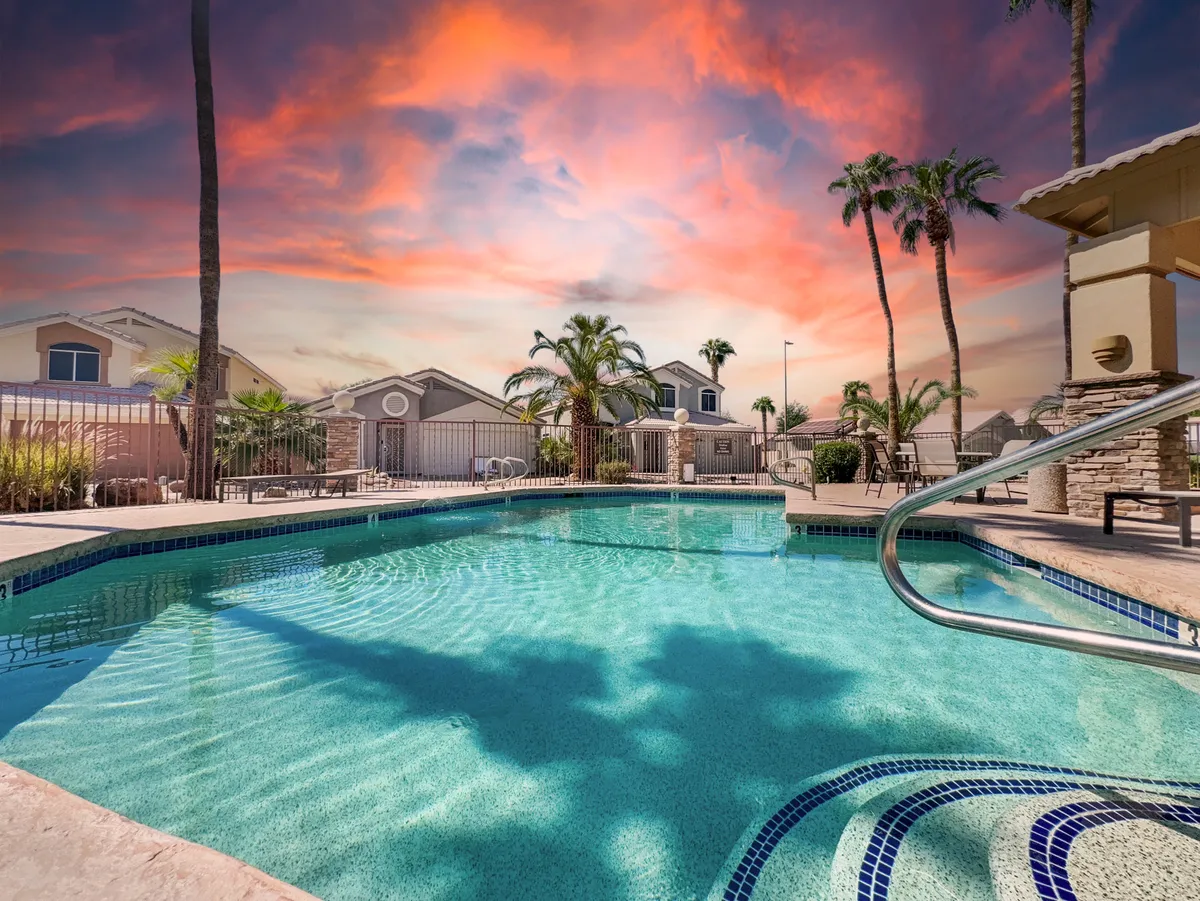 A vibrant community pool surrounded by palm trees, lounge chairs, and a colorful sunset sky, creating a resort-like atmosphere just steps from the home.