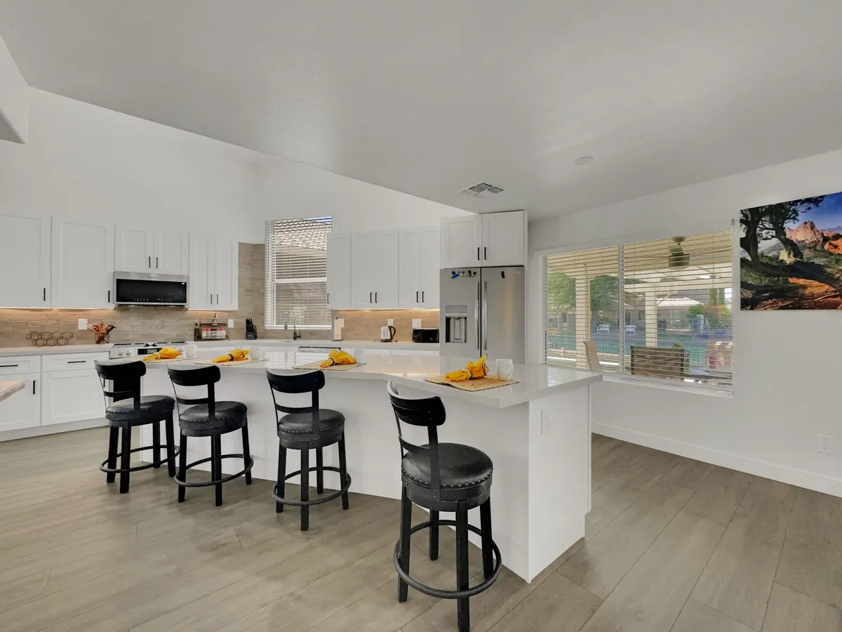 A contemporary kitchen scene with a prominent island and bar stools, surrounded by updated kitchen appliances and windows offering plenty of natural light. Subtle decor and artwork on the walls complete the welcoming ambiance, suggesting a space used for both cooking and entertaining.