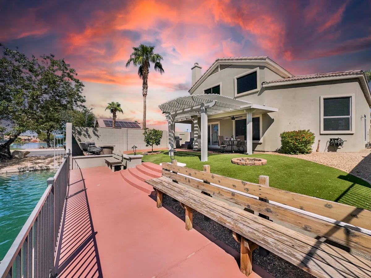 A serene backyard seating area with a fire pit, comfortable outdoor chairs, palm trees, and a scenic waterfront in the background. The setting is perfect for outdoor dining, evening gatherings, or simply relaxing by the water as the sun sets.