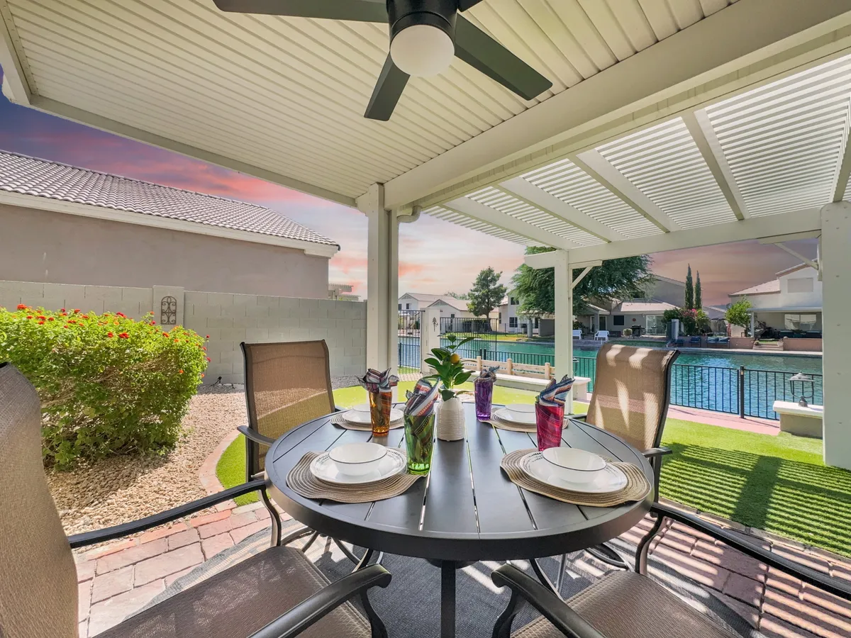 An inviting outdoor patio with a table set for dining, with a swimming pool and lush green hedge in the background. The space is arranged for group gatherings and relaxation after a big game or event.