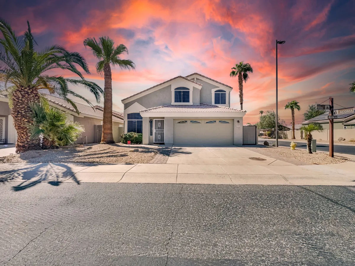 A welcoming front view of the home framed by palm trees, with vibrant sunset hues painting the sky. The inviting facade signals a peaceful, friendly neighborhood perfect for evening strolls or garden chats.