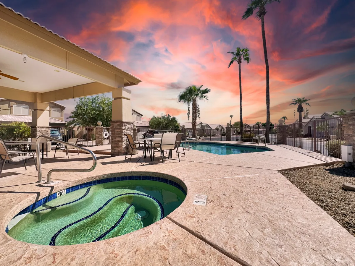 An inviting outdoor area featuring a sparkling swimming pool, a bubbling jacuzzi, palm trees, and ample seating for relaxation or socializing. The space exudes a luxurious, resort-like atmosphere perfect for unwinding after work.